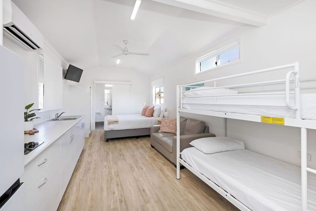A compact, modern room with bunk beds, a kitchenette, and a ceiling fan.