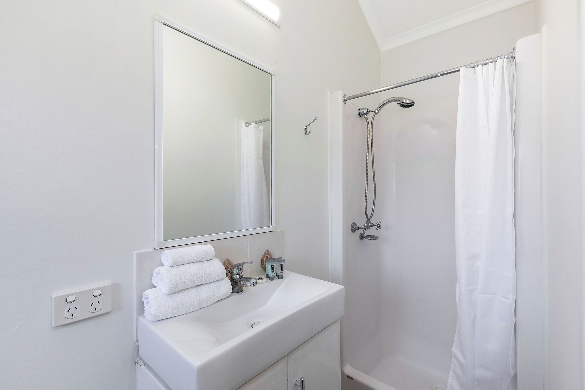 A bathroom with a white sink, a mirror, a shower with a curtain, and a towel rack.