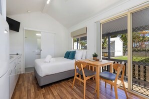 A compact room with a bed, a small table, and a chair. There is a sliding glass door leading to an outdoor area with a view of a house and greenery. - Reflections Ballina - Holiday Park (Ballina)