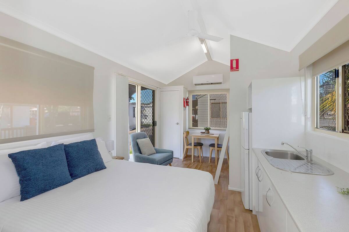 A bedroom with a bed, a desk, and a kitchenette.