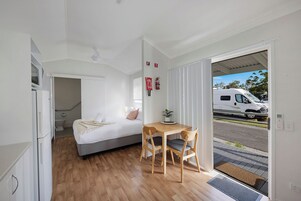 Un dormitorio con cama, mesita de noche y vistas a la calle a través de una puerta abierta.