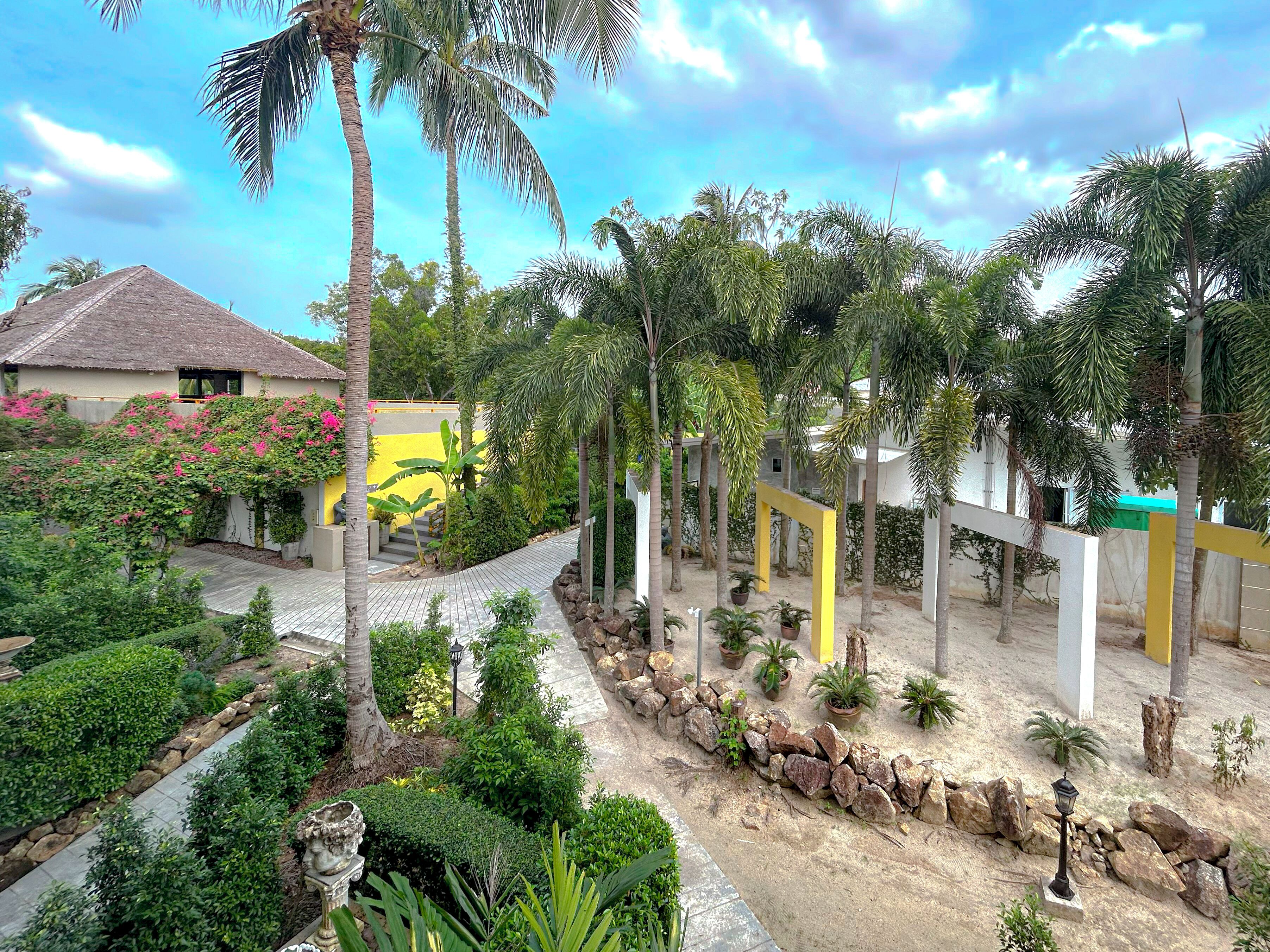 Un jardín tropical con un sendero, palmeras y un edificio amarillo.