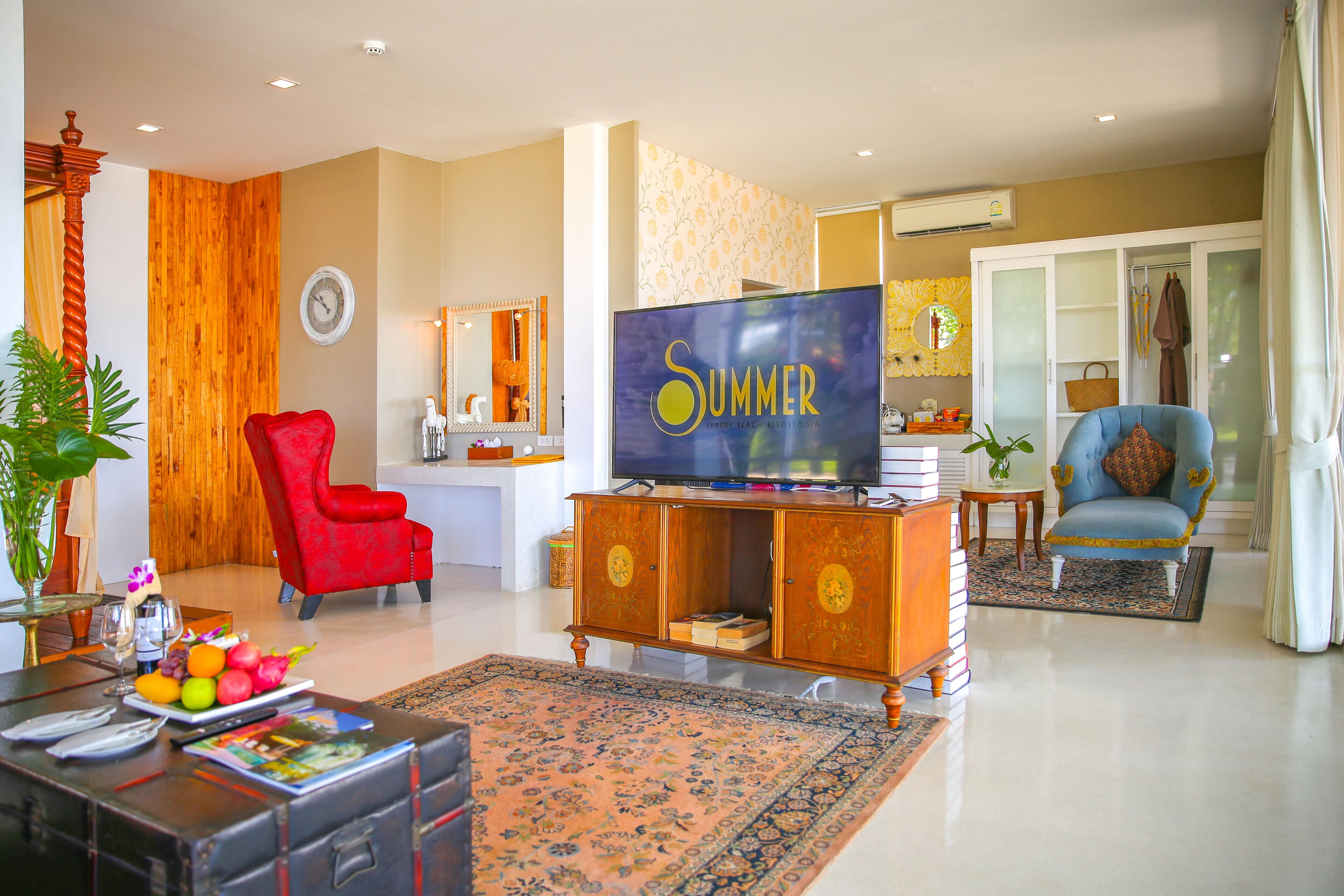 A living room with a television, red and blue chairs, a wooden cabinet, and a large rug.