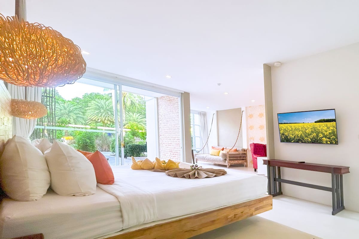 Une chambre moderne avec un grand lit, une plateforme en bois, un téléviseur et une vue sur un champ de fleurs jaunes.