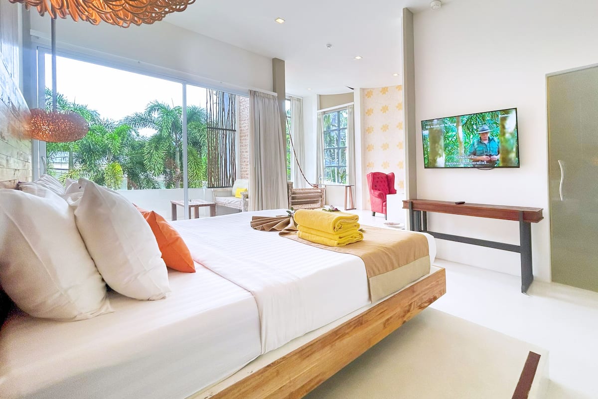 Une chambre d’hôtel moderne avec un grand lit, une télévision et une vue sur la verdure environnante.
