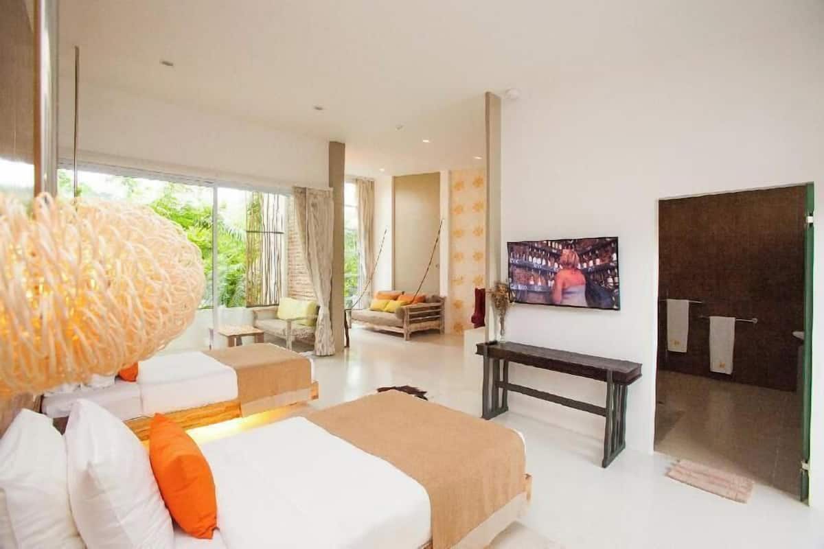 Une chambre d’hôtel moderne avec un grand lit, un banc, une télévision et une vue sur la verdure environnante.