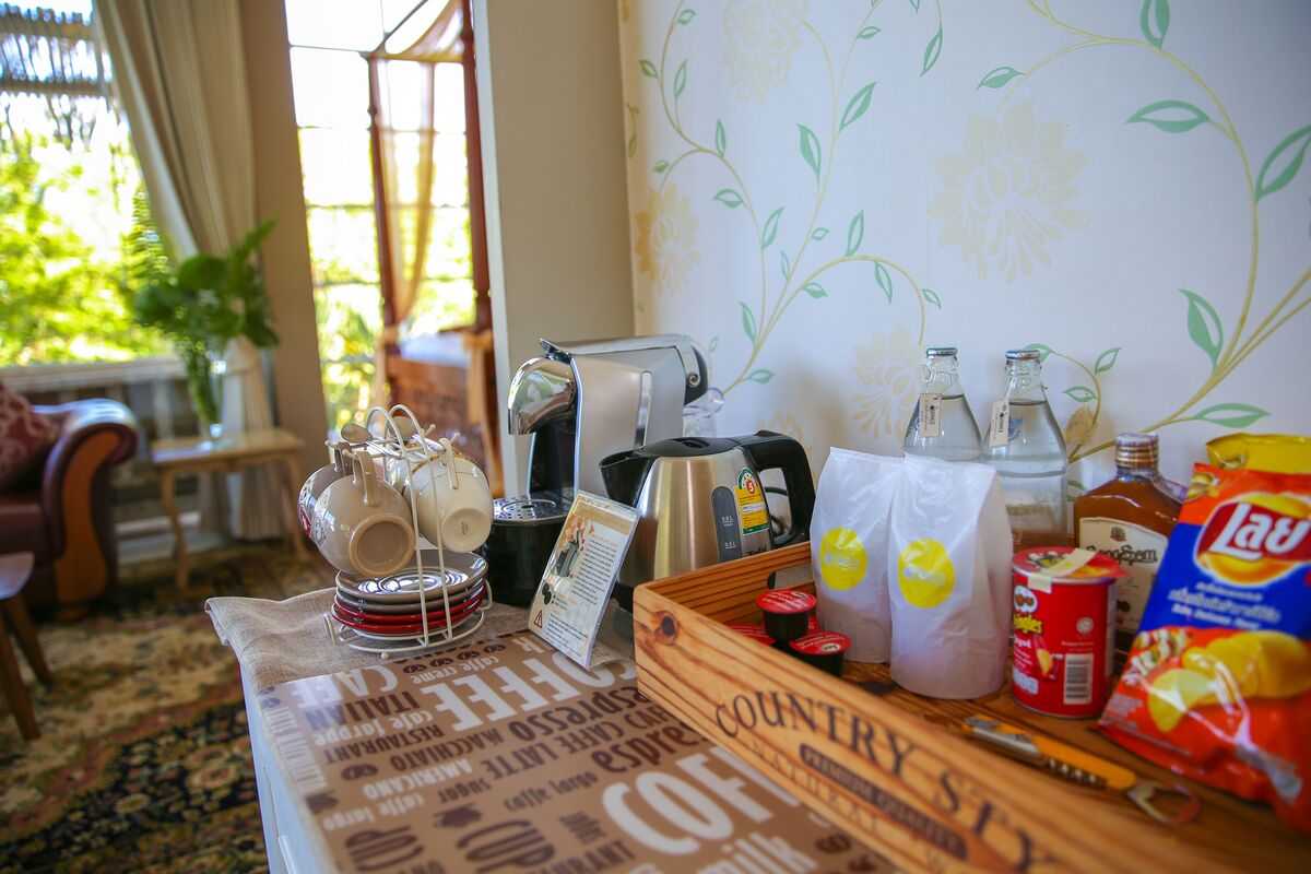 A table with coffee-making equipment, bags of coffee, and snacks in a cozy room with floral wallpaper and a view of greenery outside.
