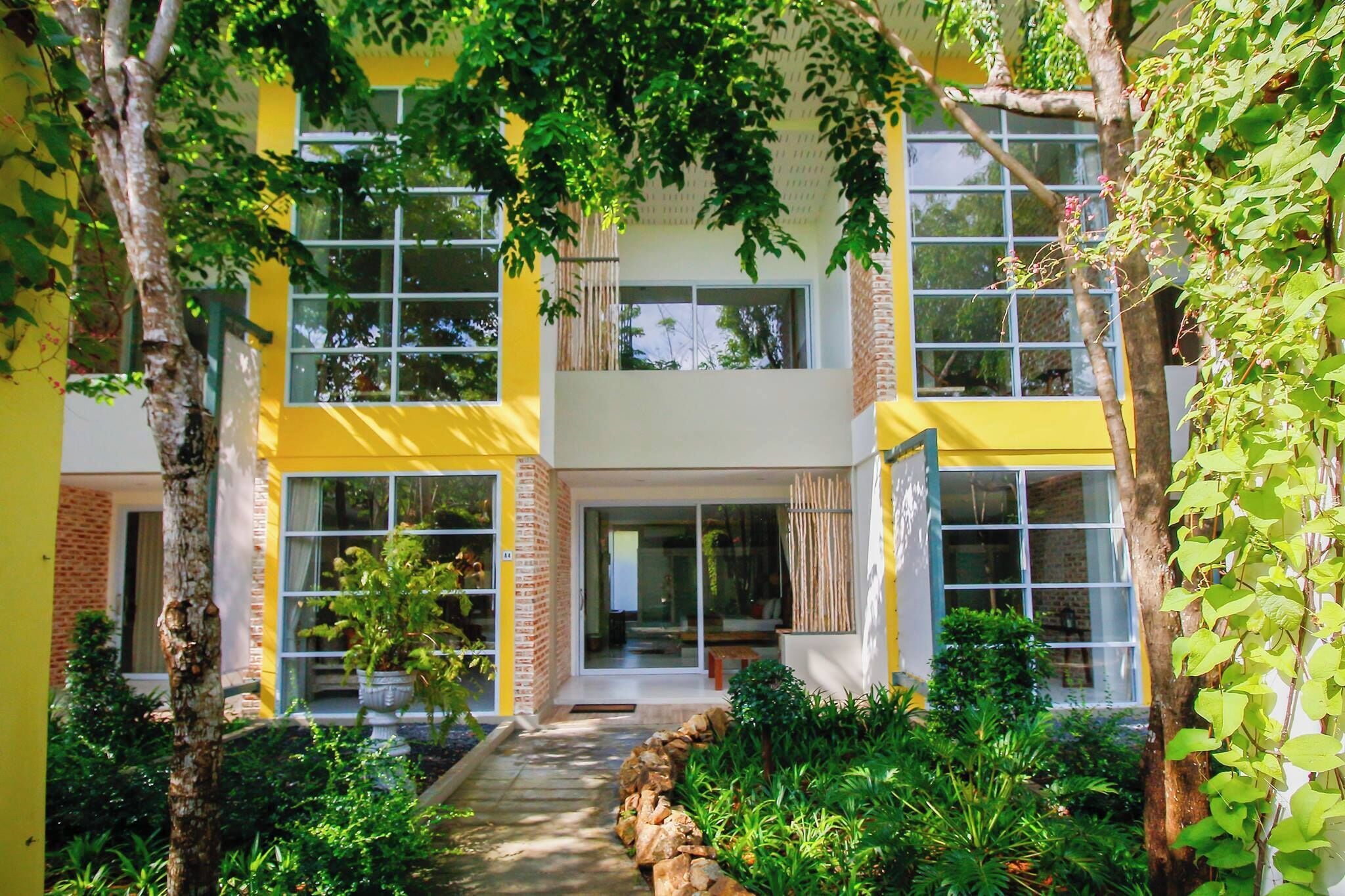 A modern yellow building with large windows and a garden area with various plants and a stone pathway.