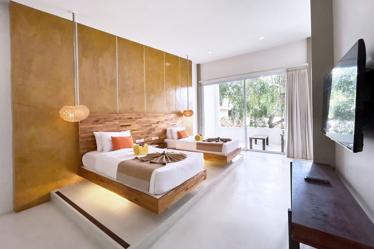 Une chambre moderne avec un grand lit, une télévision et un balcon donnant sur la verdure.
