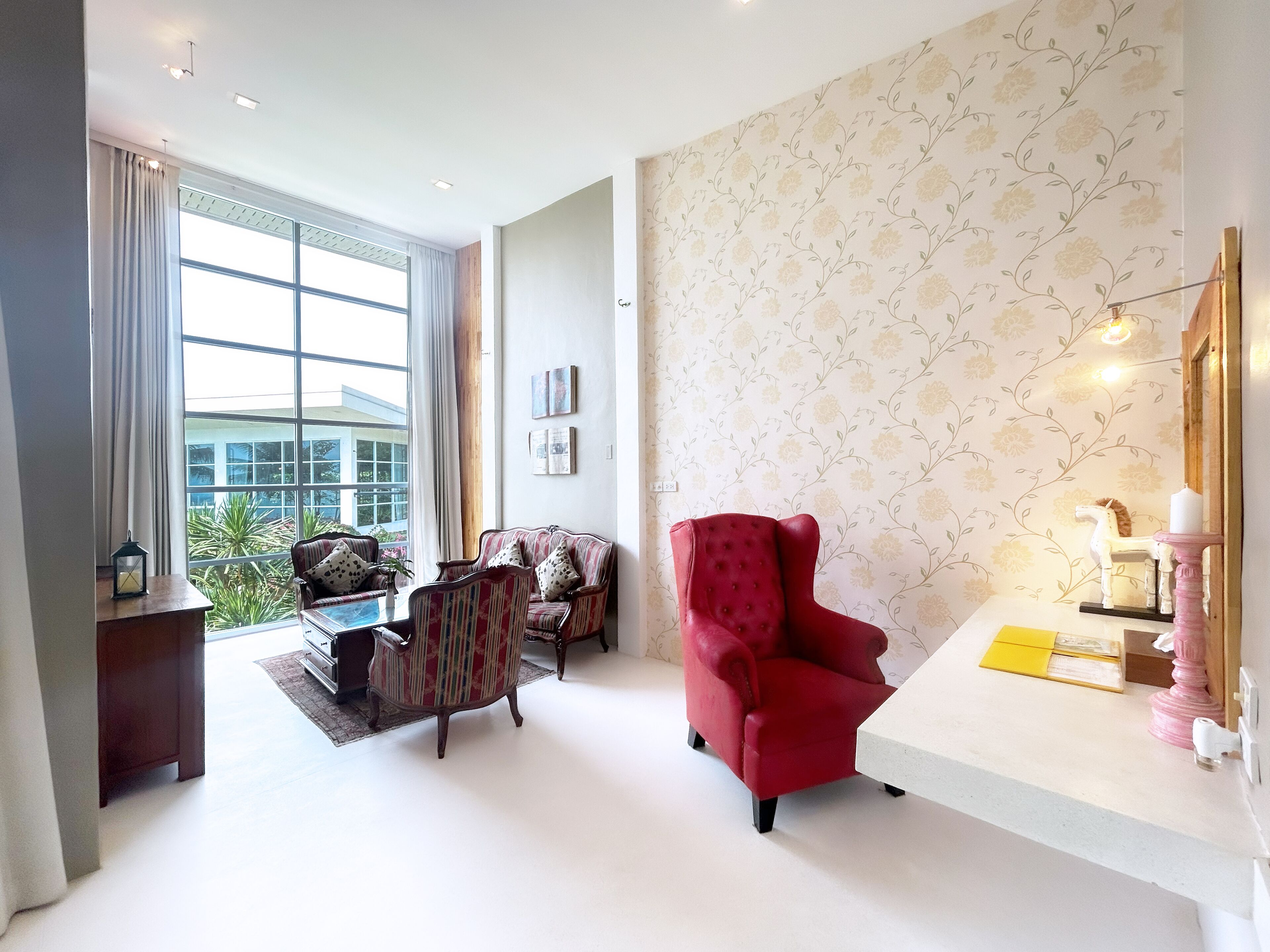 Ein modernes Wohnzimmer mit großem Fenster, einem roten Sessel, einem gestreiften Sofa und einem kleinen Tisch mit Lampe.