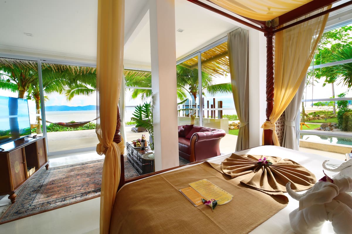 Une chambre d’hôtel dotée d’une grande fenêtre donnant sur la plage et les palmiers.