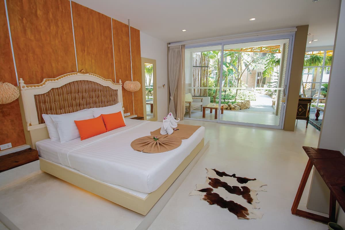 Une chambre d’hôtel moderne avec un grand lit, une vue sur un jardin tropical et une tête de lit en bois.