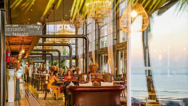 An indoor seating area with tables and chairs, a vintage bathtub, and a view of the water outside. - Summer Luxury Beach Resort and Spa (Ko Pha-ngan)