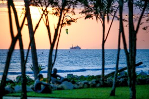A sunset view with a ship in the distance, trees in the foreground, and a person sitting on the grass. - Summer Luxury Beach Resort and Spa (Ko Pha-ngan)