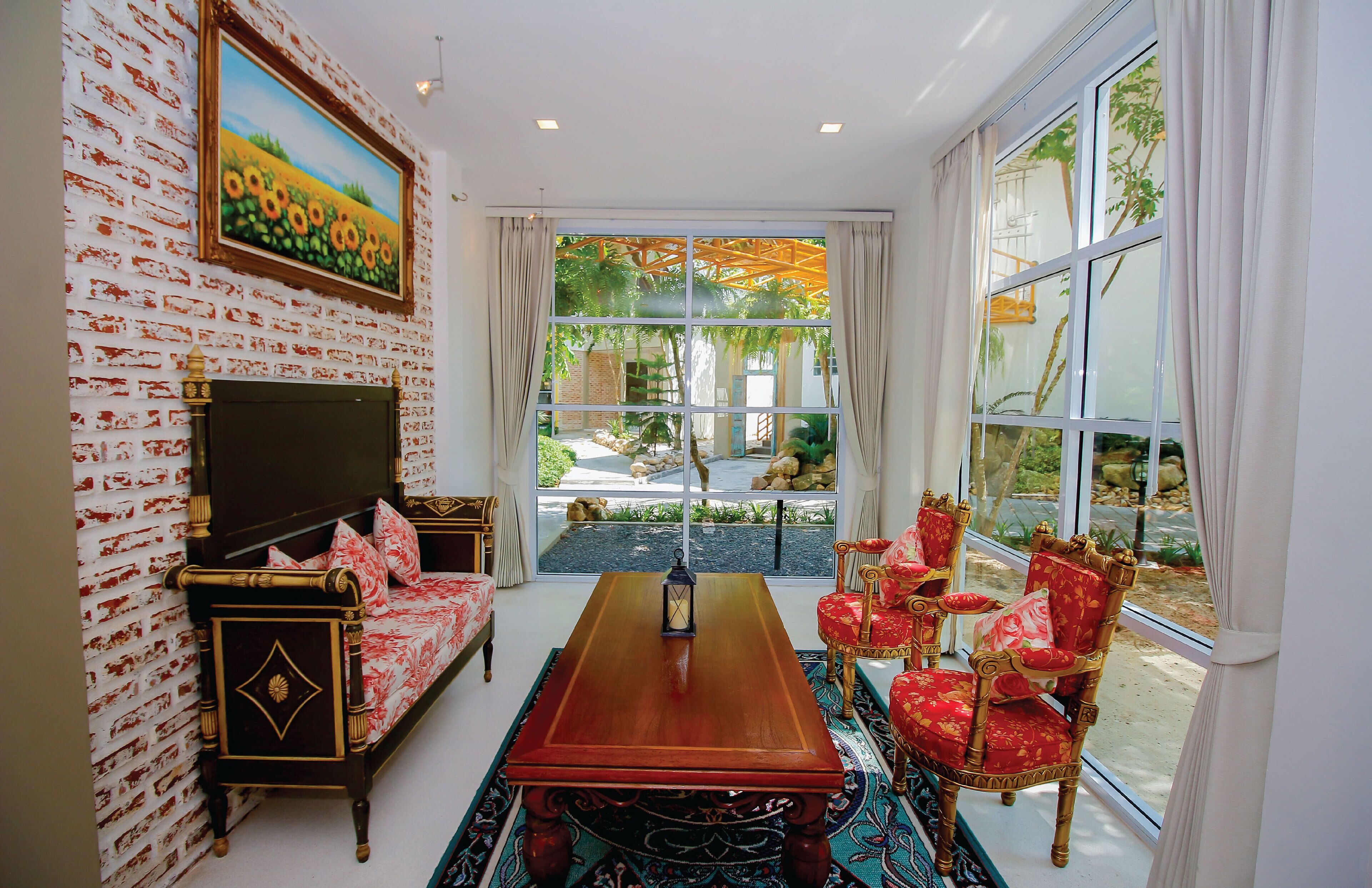 A room with a wooden table, red upholstered chairs, a sofa, and a TV against a brick wall.