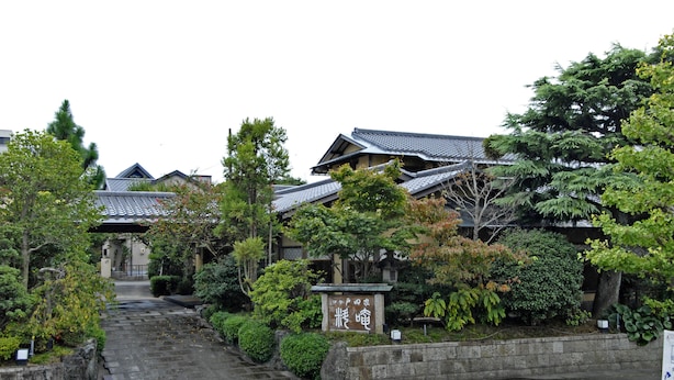 A traditional Japanese building with a tiled roof, surrounded by lush greenery and a stone pathway leading to the entrance. - Ise Todaya Ryoan (Ise)