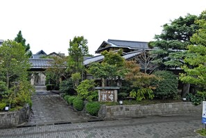 A traditional Japanese building with a tiled roof, surrounded by lush greenery and a stone pathway leading to the entrance. - Ise Todaya Ryoan (Ise)