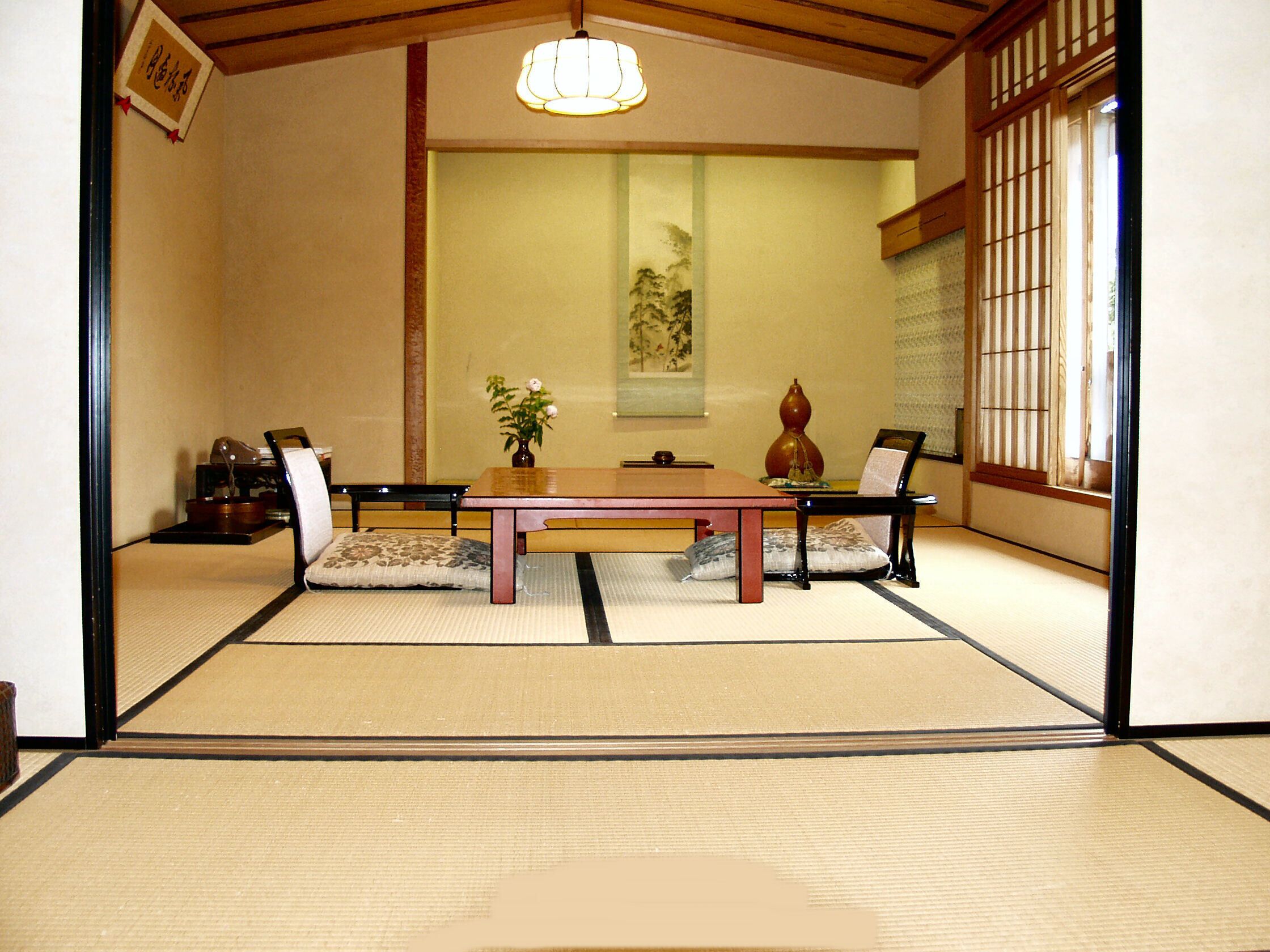 A tatami mat room with a low table, chairs, a vase, and a hanging scroll.