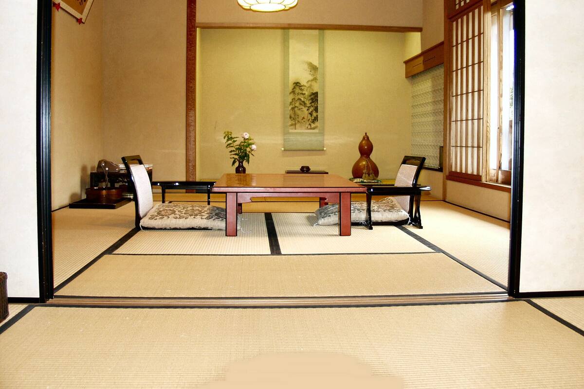 A tatami mat room with a low table, chairs, a vase, and a hanging scroll.