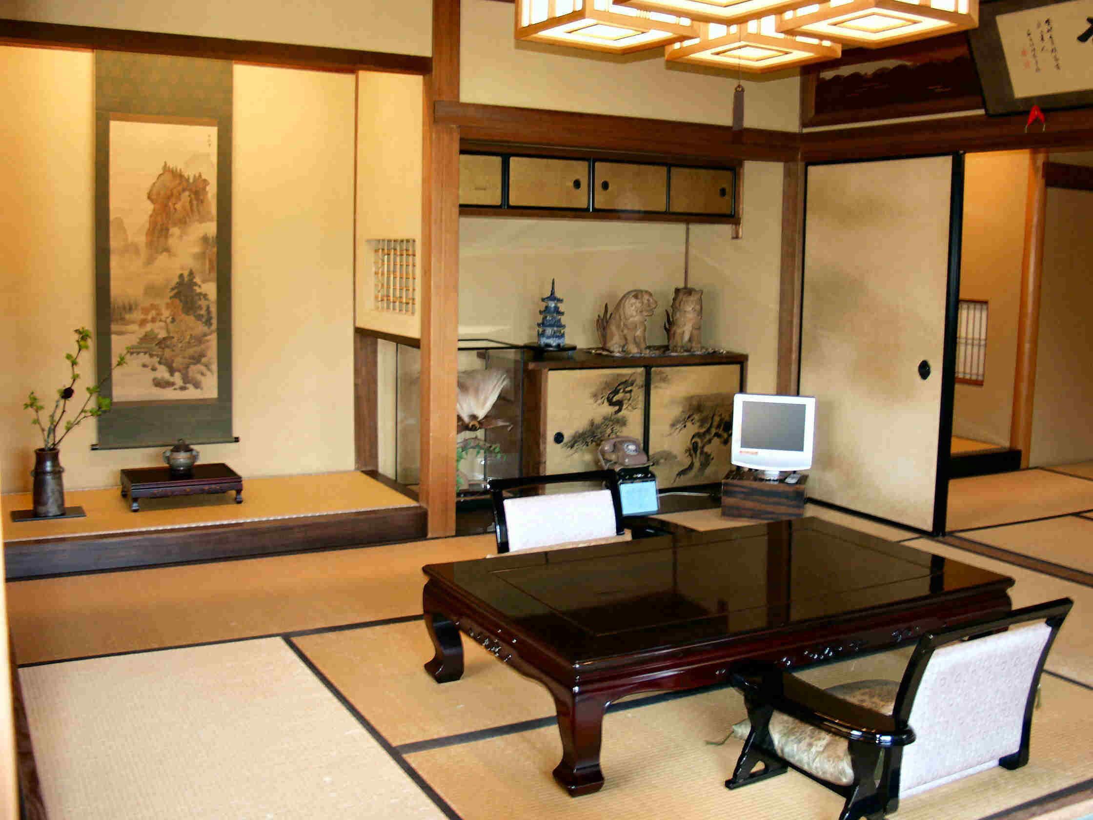 Een traditionele Japanse kamer met tatami vloeren, een lage tafel, stoelen, een televisie en diverse decoratieve objecten.