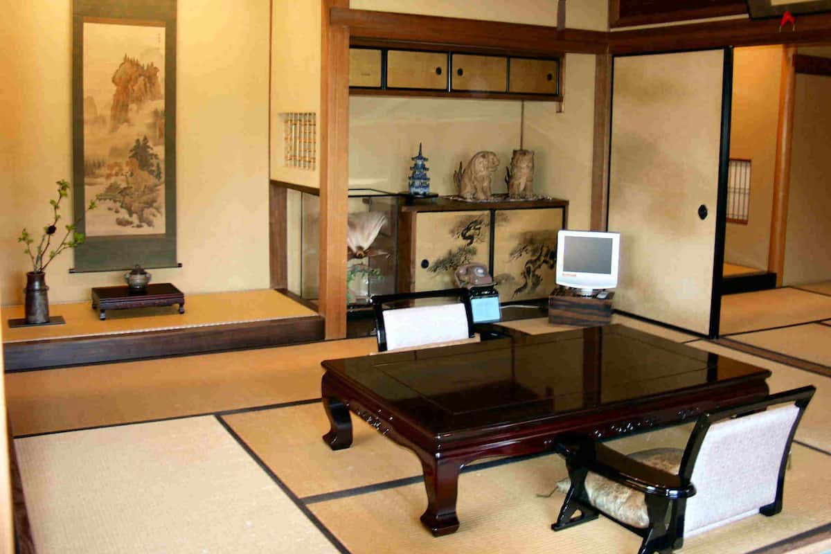 A traditional Japanese room with tatami flooring, a low table, chairs, a television, and various decorative items.