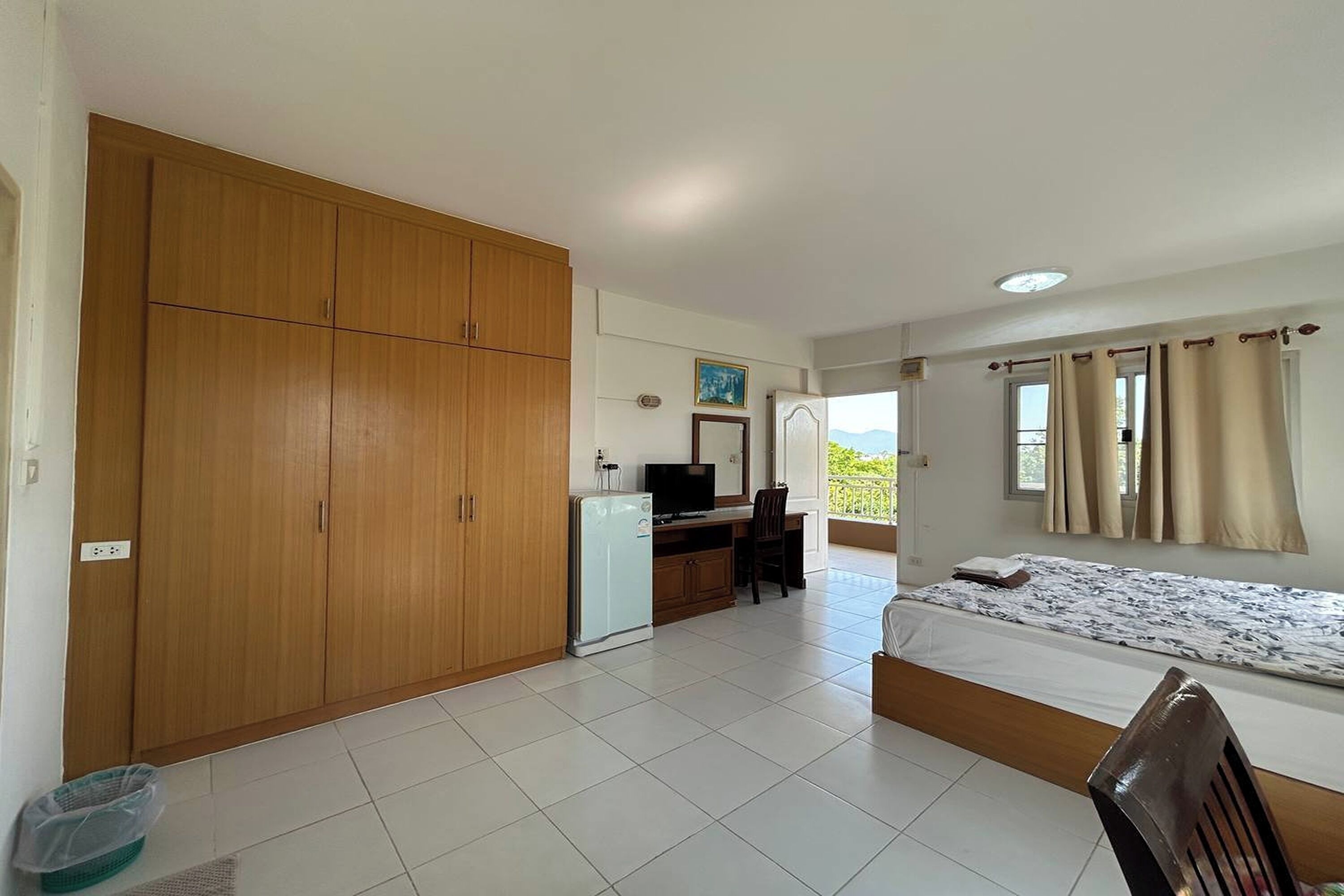 A bedroom with a bed, a desk, a wardrobe, and a balcony with curtains.