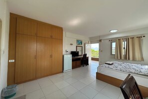 Een slaapkamer met een bed, een bureau, een kledingkast en een balkon met gordijnen.