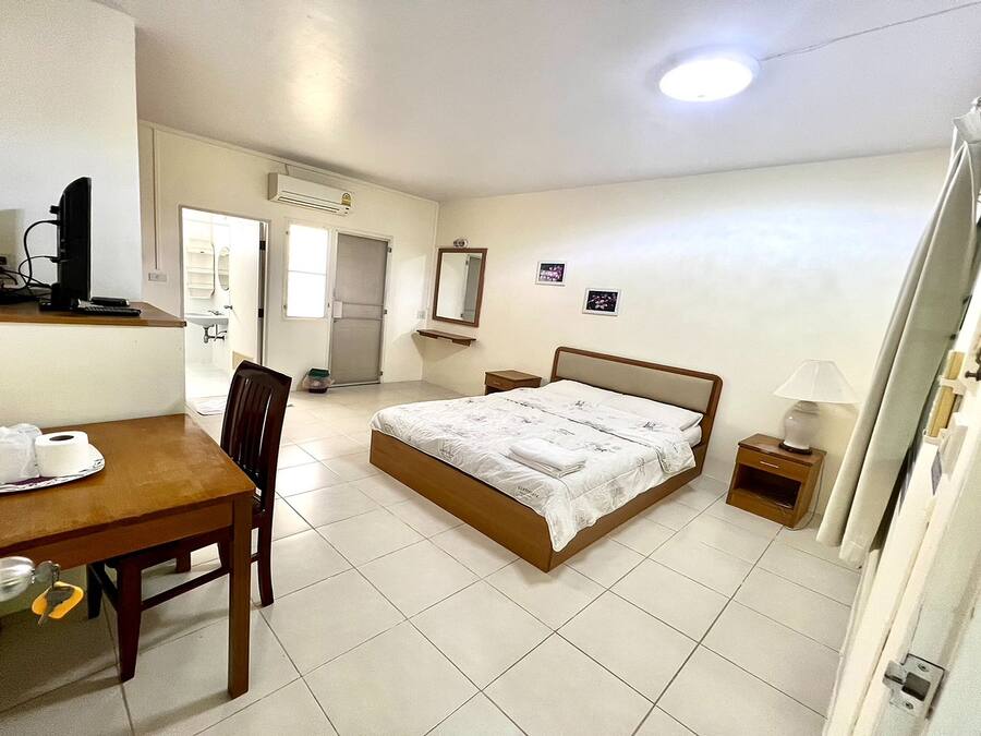 A hotel room with a bed, a desk with a chair, a small table with a lamp, and a television.