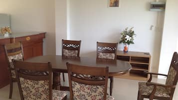 A dining area with a round wooden table surrounded by six chairs with floral upholstery. There is a wooden sideboard and a vase with flowers on a table to the right.