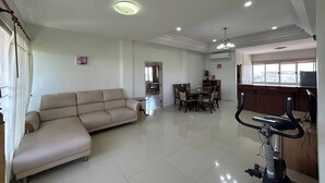 A spacious living room with a beige sofa, a dining area with a table and chairs, and a stationary exercise bike. - U.D.Home Apartment (Ban Chang)