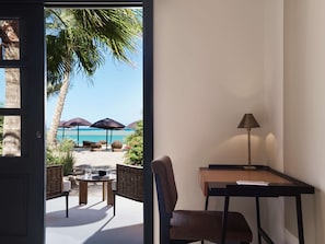 Enjoy a serene beach view from the large window, relax in the comfortable seating area, and work at the simple desk with a lamp.