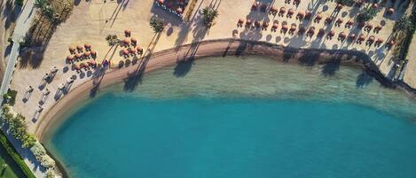An aerial view of a beach resort with a clear blue pool, sun loungers, and palm trees.