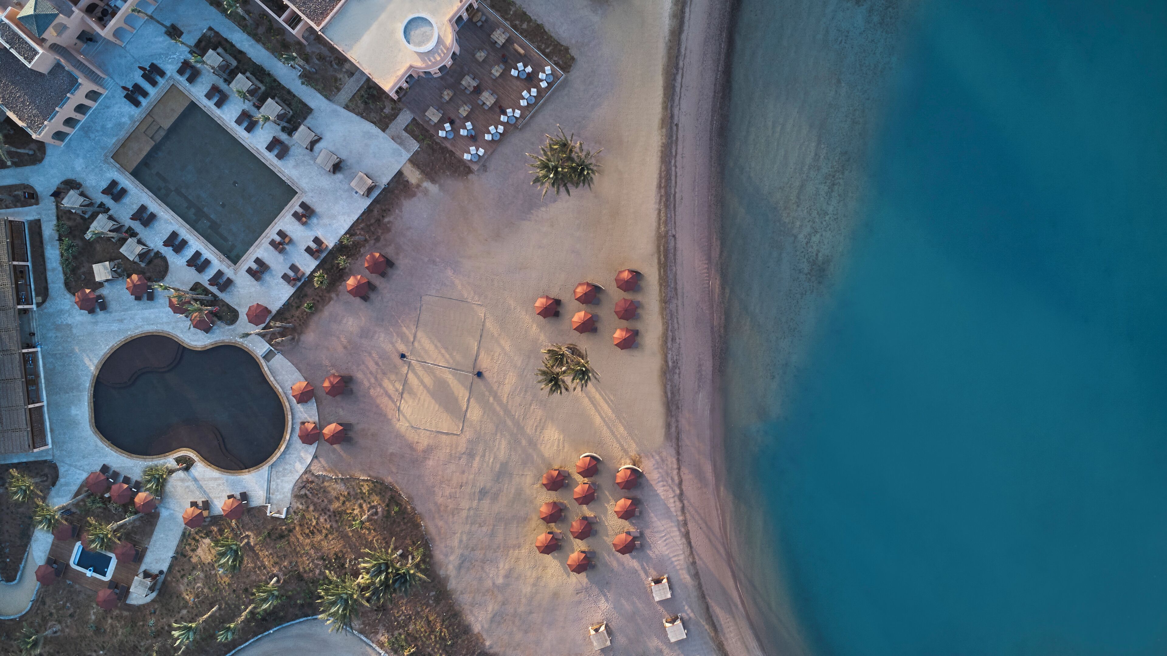 An aerial view of a resort with a pool, beach area, and beach umbrellas.