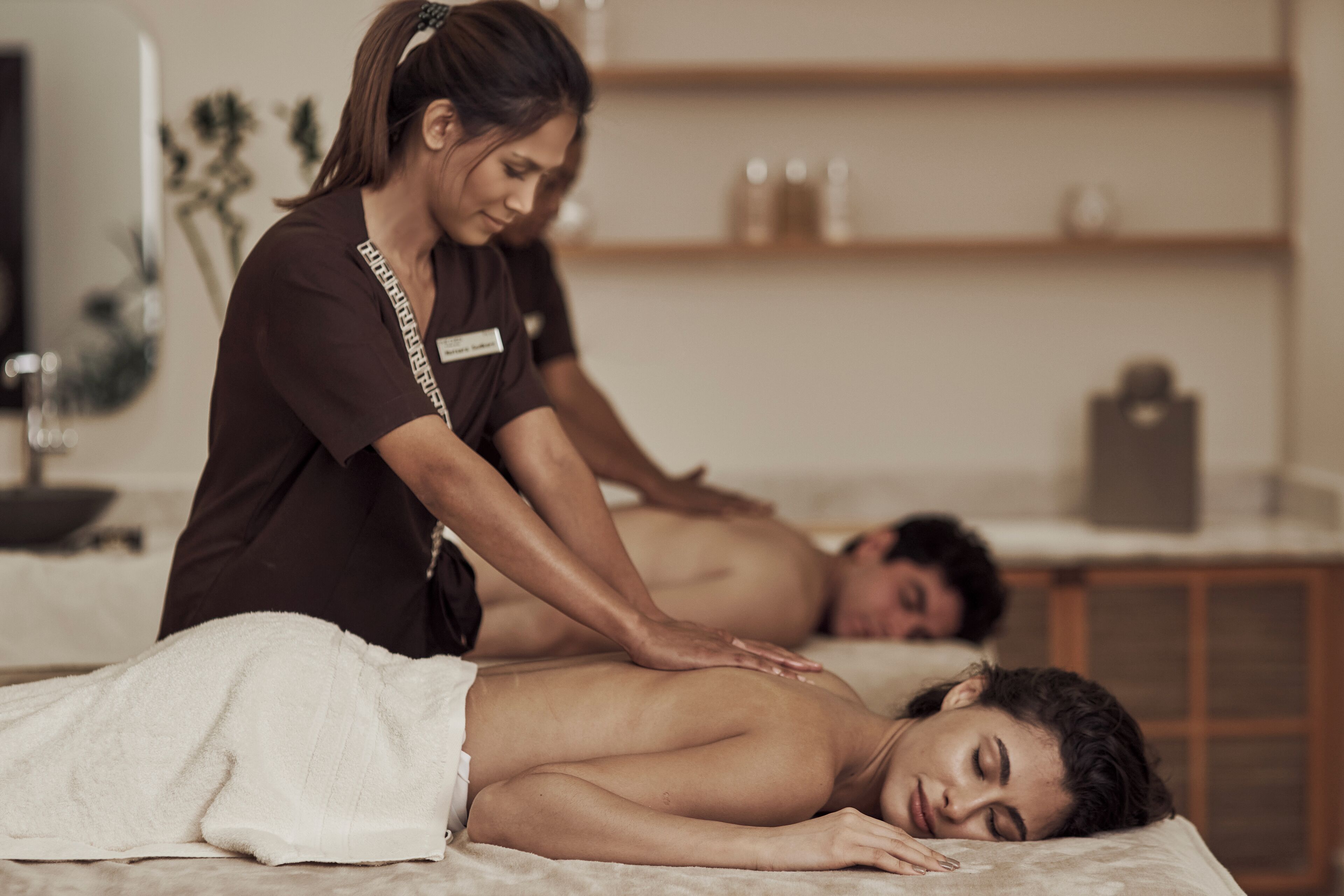 A massage therapy room with a massage table, a towel, and a shelf with bottles in the background.