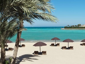 Uma praia com palmeiras, cadeiras de praia e guarda-sóis.