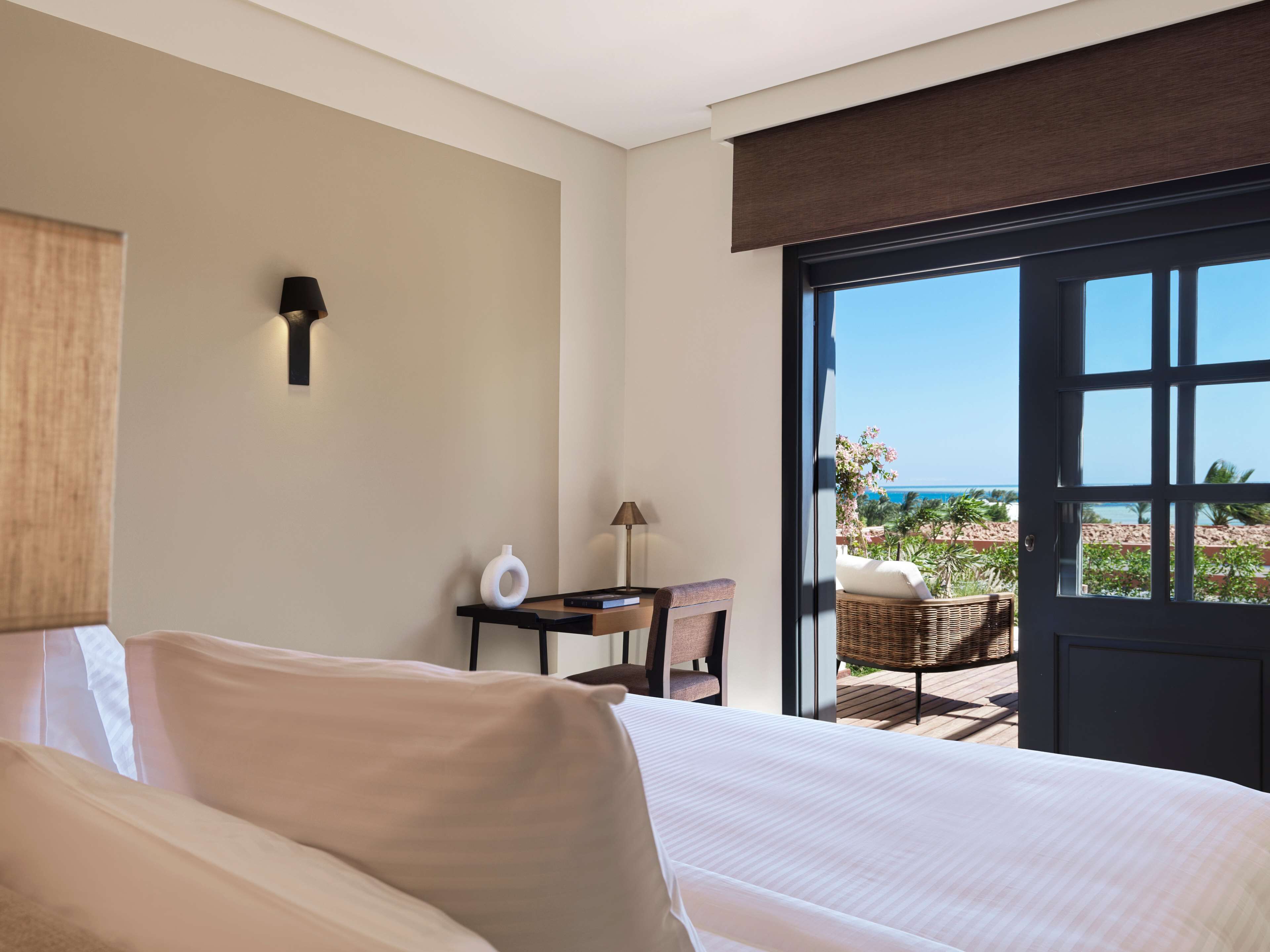 A hotel room with a bed, a desk, a chair, and a view of the ocean.