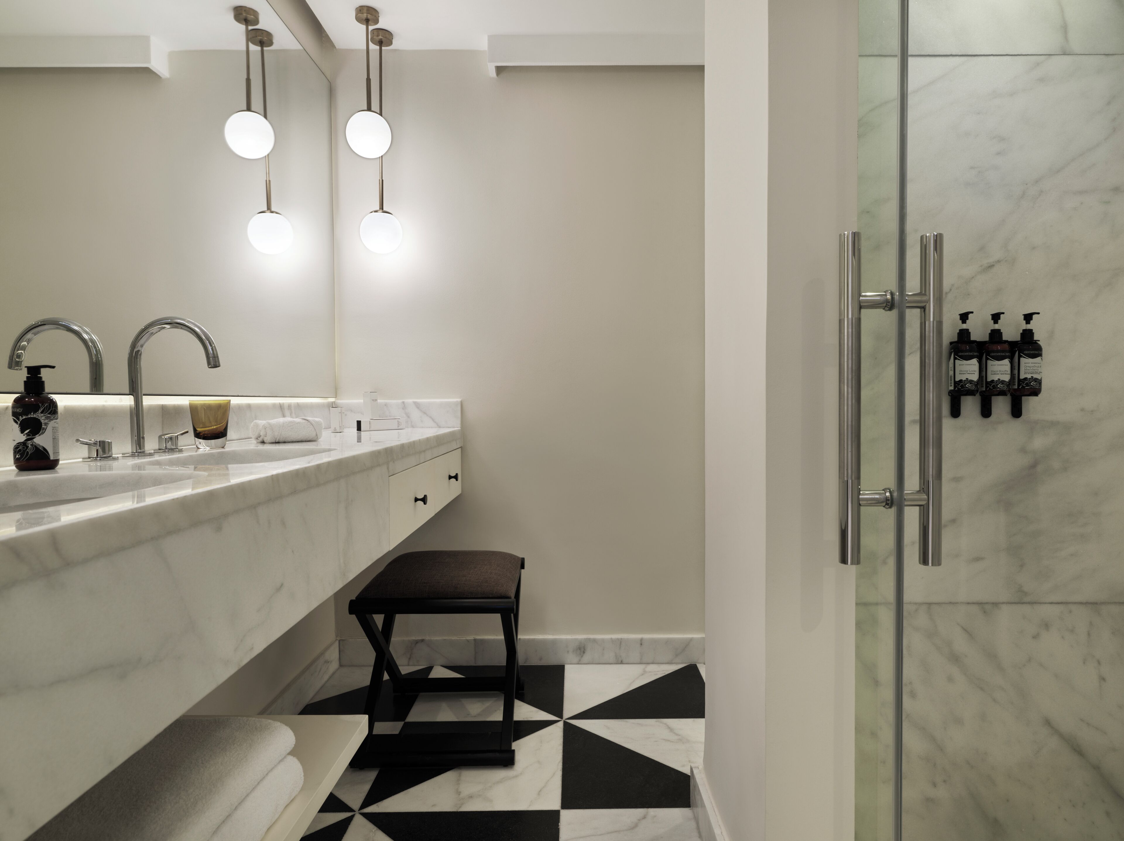A modern bathroom with a marble sink, two round lights, a glass shower enclosure, and a black and white tiled floor.