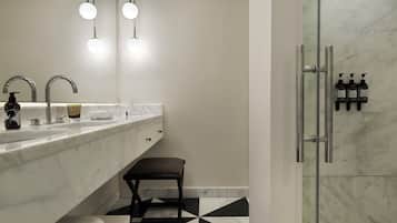 A modern bathroom with a marble sink, two round lights, a glass shower enclosure, and a black and white tiled floor.