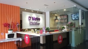 Een hotel receptiebalie met een bordje met de tekst 'D'Metro Hotel'. Er zijn twee rode borden met de tekst 'ZEN ROOMS' en 'OYO'.