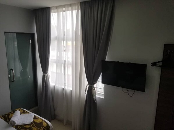 Una habitación de hotel con cama, televisor montado en la pared y ventana con cortinas.