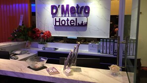 Een receptiebalie bij Hotel D'Metro, met een marmeren toonbank, een groot bord en voorzieningen zoals een telefoon, een mand en een vaas met bloemen.