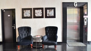 Een hal met twee zwarte fauteuils, een klein rond tafeltje met een boek, en drie ingelijste bloemwerken aan de muur.