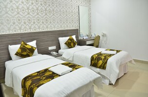 Habitación de hotel con dos camas, cada una con ropa blanca y un diseño decorativo de pan de oro. Hay un escritorio con una silla, un teléfono y un espejo.
