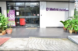 L'ingresso dell'Hotel D'Metro con una porta in vetro, piante in vaso e un cartello promozionale.