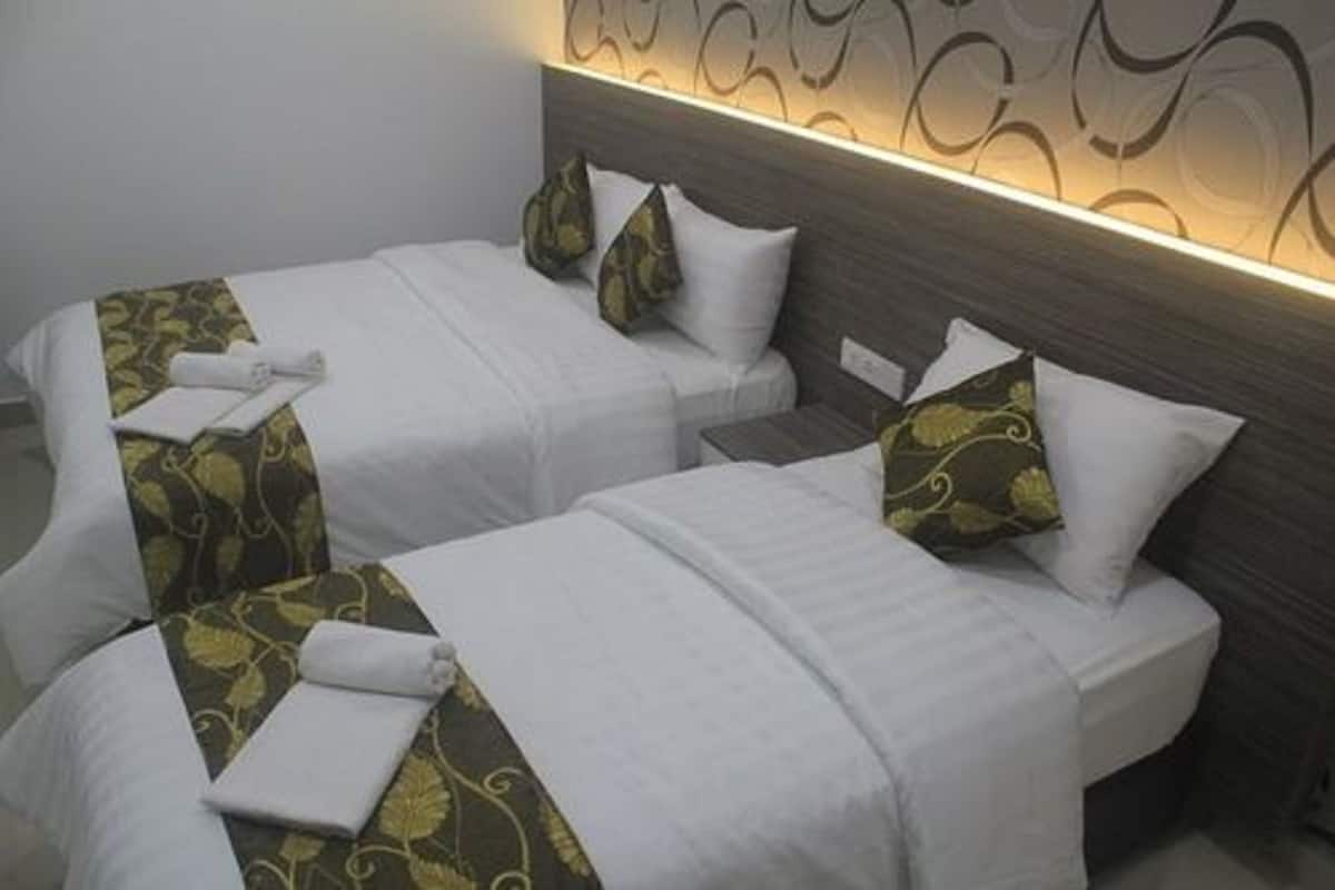Dos camas individuales con ropa de cama blanca y almohadones verdes estampados, un cabecero de madera y una pared con un diseño circular.