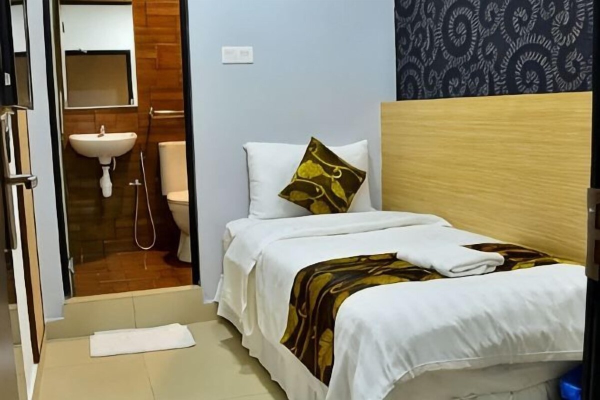 Habitación de hotel con cama, cabecera de madera, almohada blanca, toalla, lavabo y espejo.