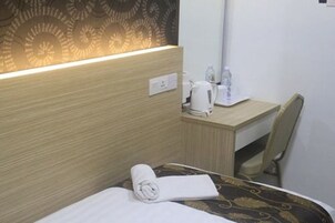 Une chambre d’hôtel comprenant un lit, un bureau, une chaise, une lampe et un mur orné d’un motif décoratif.