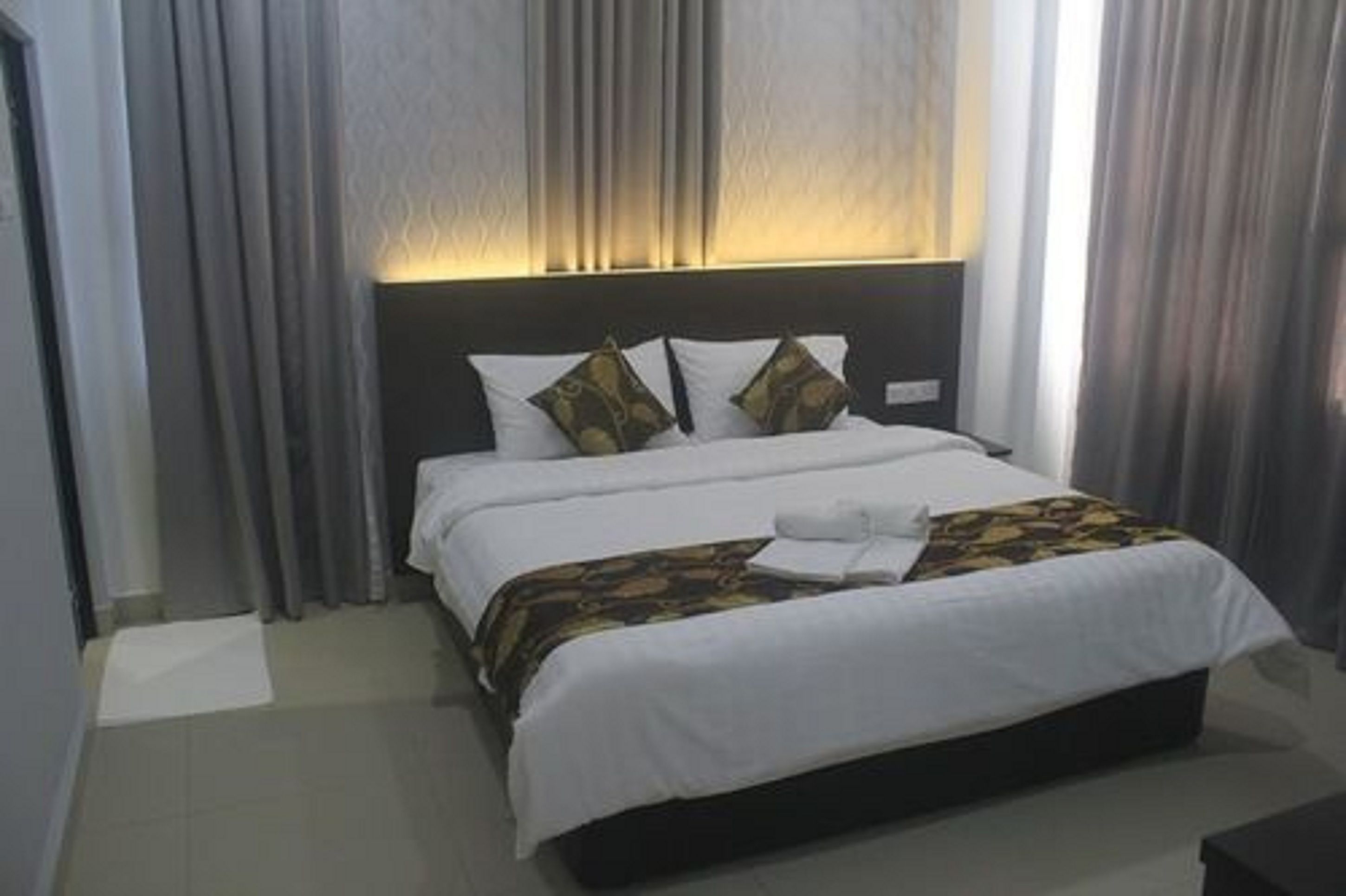 Een hotelkamer met een groot bed, twee kussens, een nachtkastje en een raam met gordijnen.