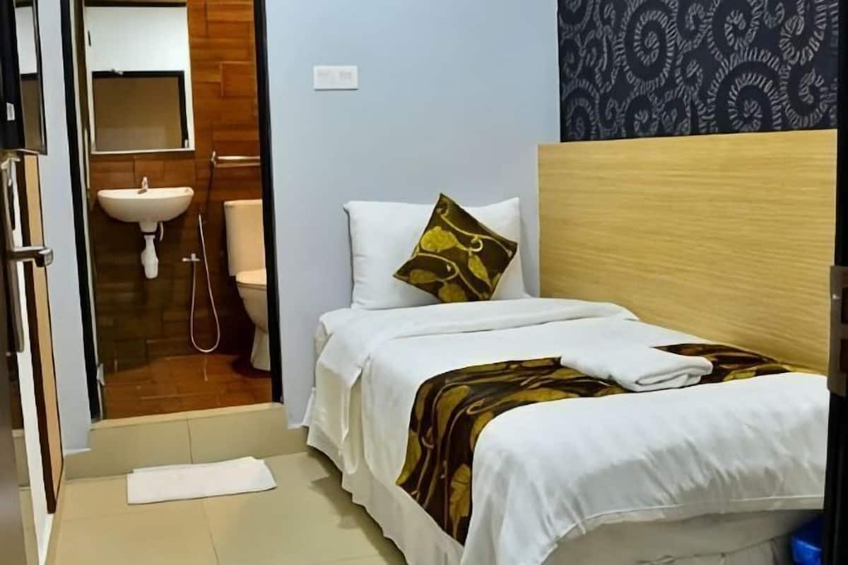 Habitación de hotel con cama, cabecera de madera, almohada blanca, toalla, lavabo y espejo.