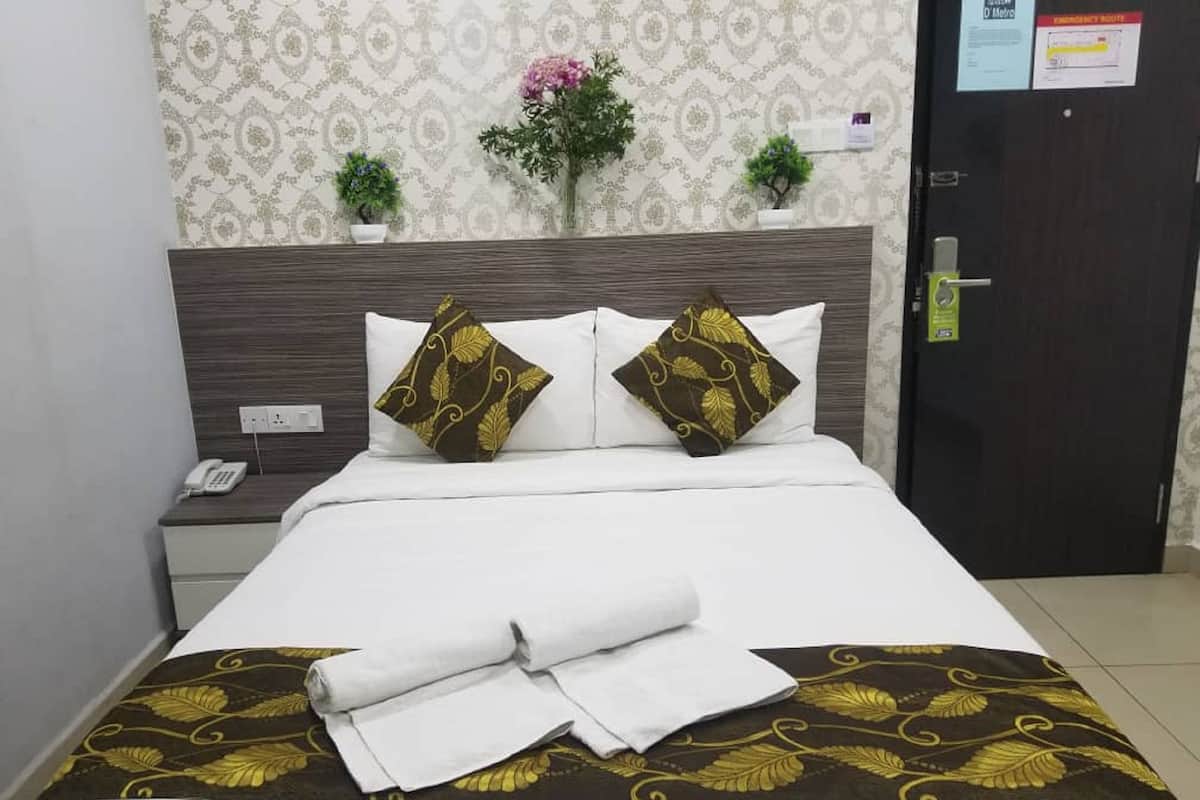 Una cama bien hecha con ropa de cama blanca y dorada, una toalla blanca doblada y dos almohadones decorativos.
